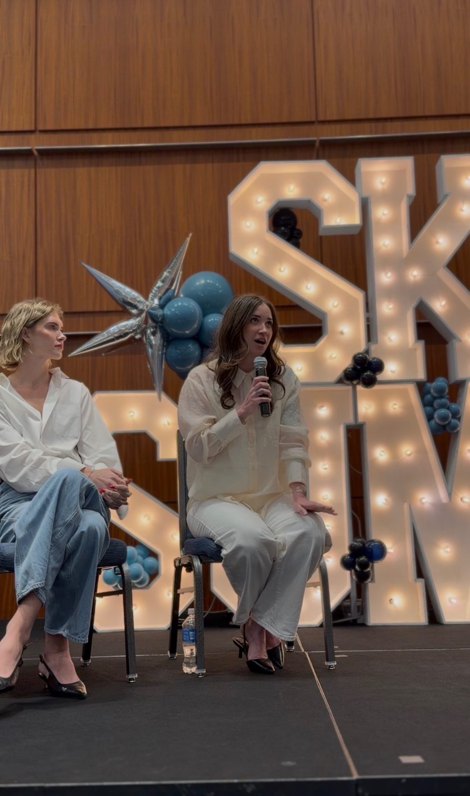 Kelly Temple speaking with a colleague on stage at the Skin Summit