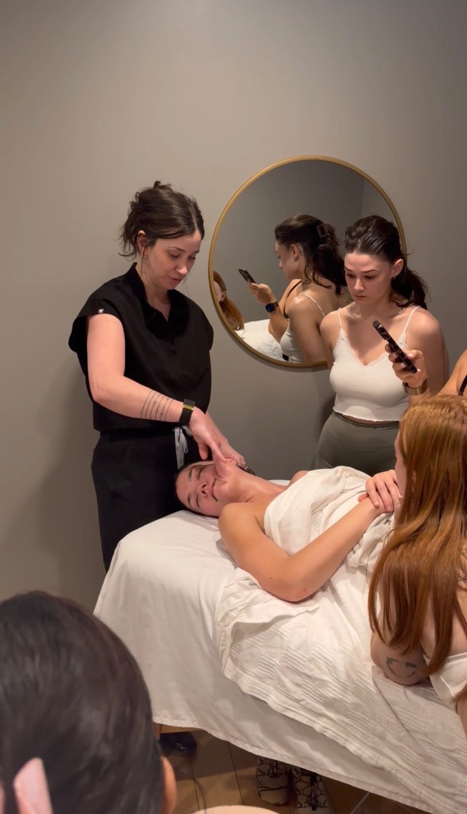 Kelly Temple guiding a student's facial massage technique while the class watches