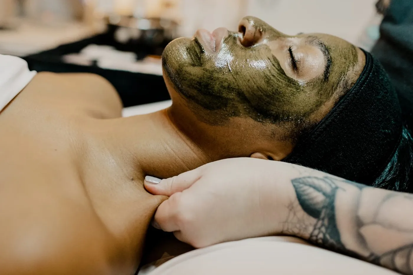 Esthetician massaging a client's neck during a facial with a botanical mask at TEMPLE