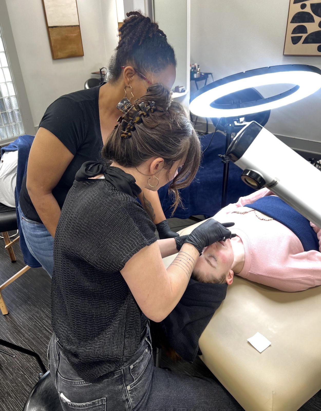 Kelly Temple demonstrating a precise facial treatment on a client under a ring light during a dermaplaning class